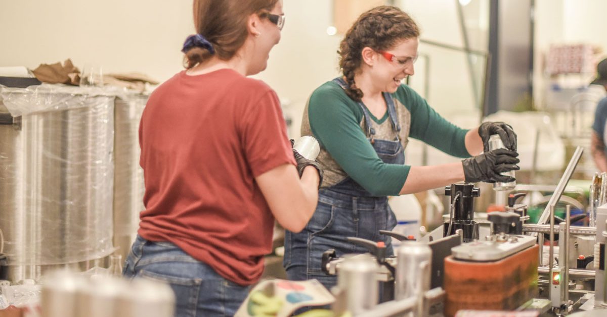 women adding labels to cans in brewery 1200x628 1